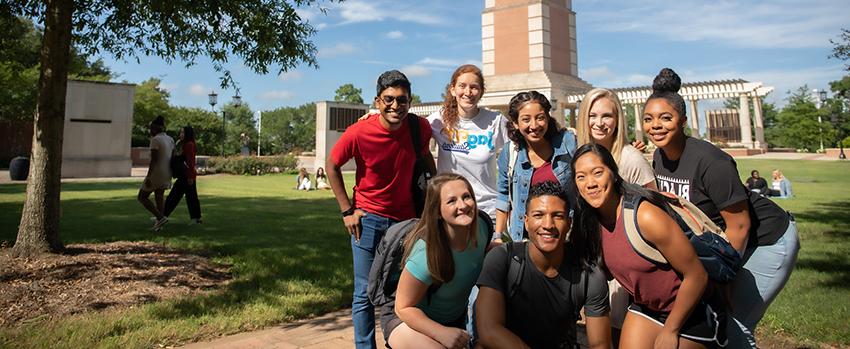A group of diverse students standing on campus in front of Moulton Tower.