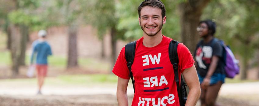 Student smiling with we are south shirt on standing outside on campus.
