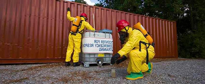 Two men in hazmat suits in front of storage container